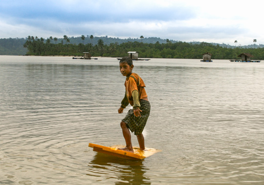 Young Mentawai boy practicing surfing on an old plastic door