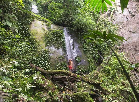 Sikerei standing by a large waterfall in the Mentawai rainforest